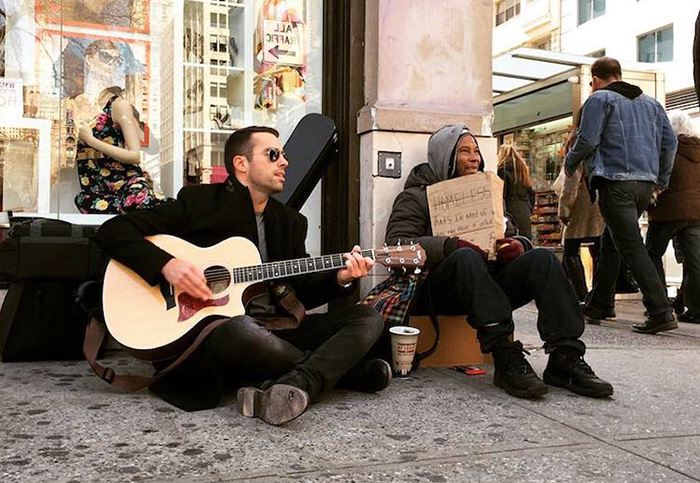 man plays guitar near homeless people to help them get money