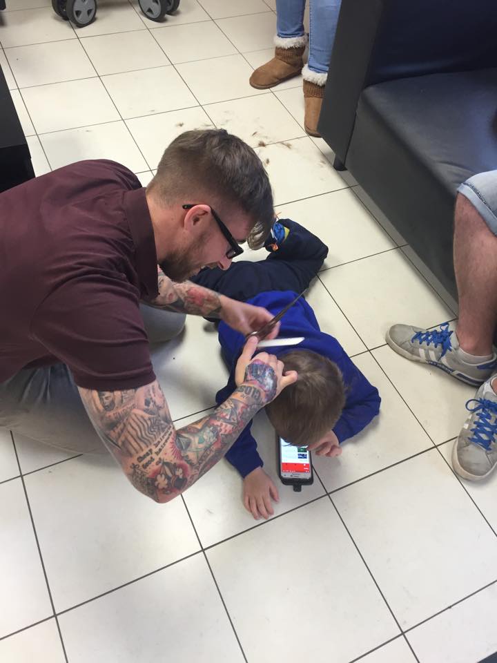 barber cuts hair on floor of boy with autism