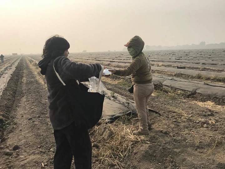 woman hands out masks to farm workers California