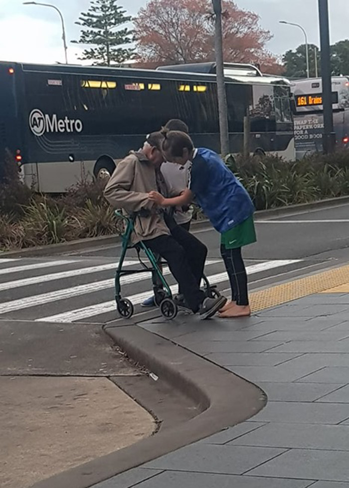 two boys help elderly man cross road